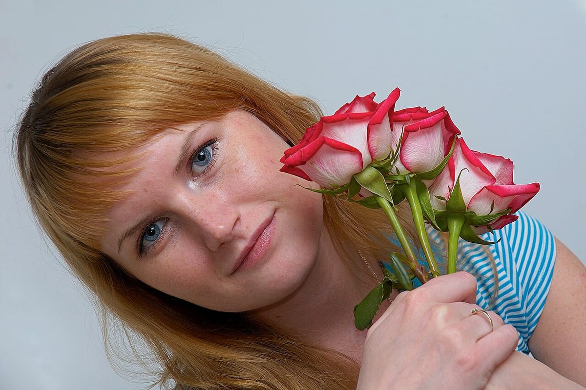 Porträt einer Frau mit rotblonden Haaren, die einen Strauß Rosen ans Gesicht hält