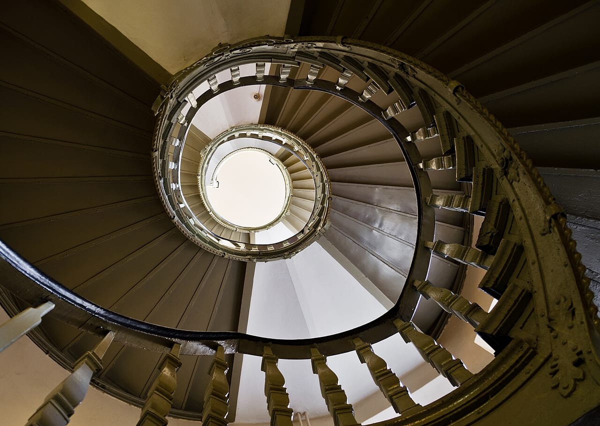 Ein Treppenhaus von unten fotografiert, die Stufen bilden eine Spirale zur hellen Öffnung