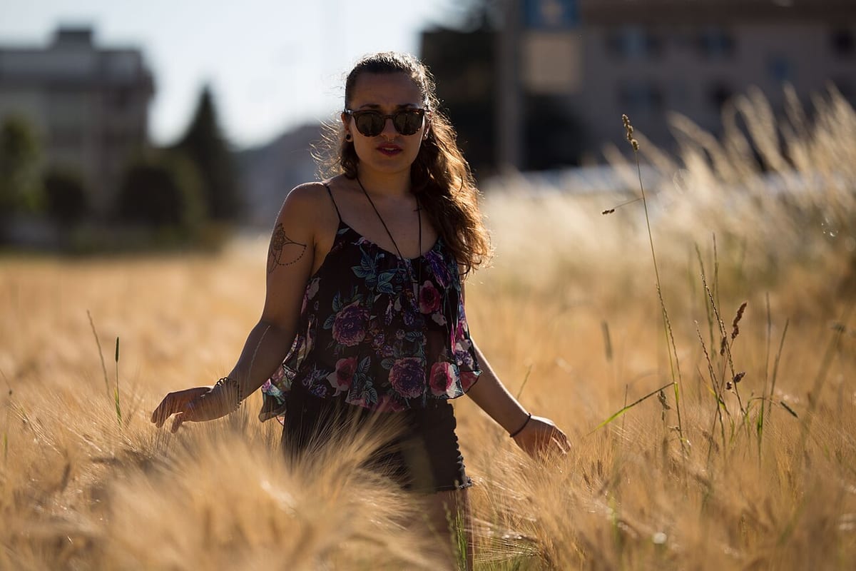 Eine Frau mit Sonnenbrille steht in einem reifen Getreidefeld und streift mit der Hand über die Ähren