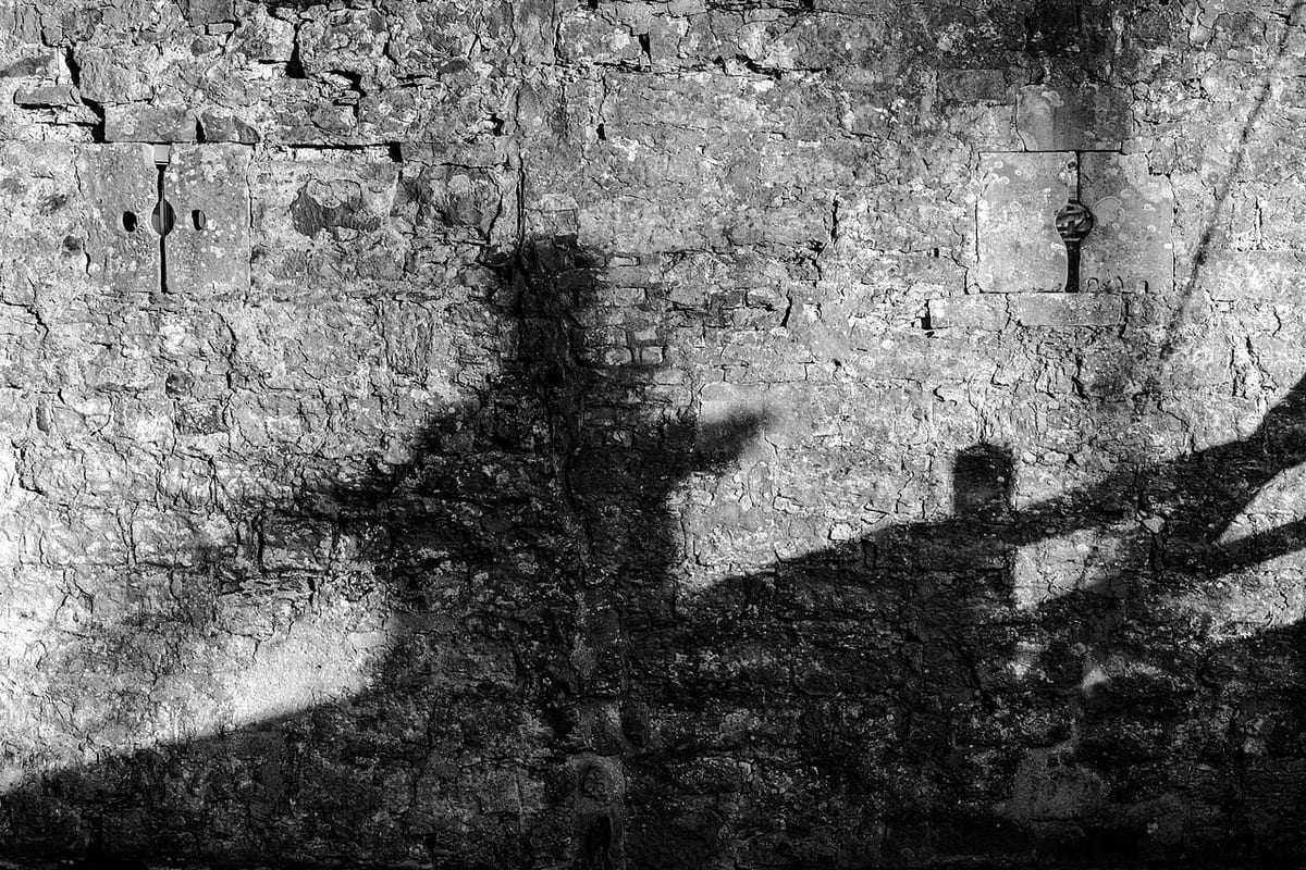 Eine verwitterte Mauer in Schwarzweiß, ein harter Schatten teilt die Fläche diagonal