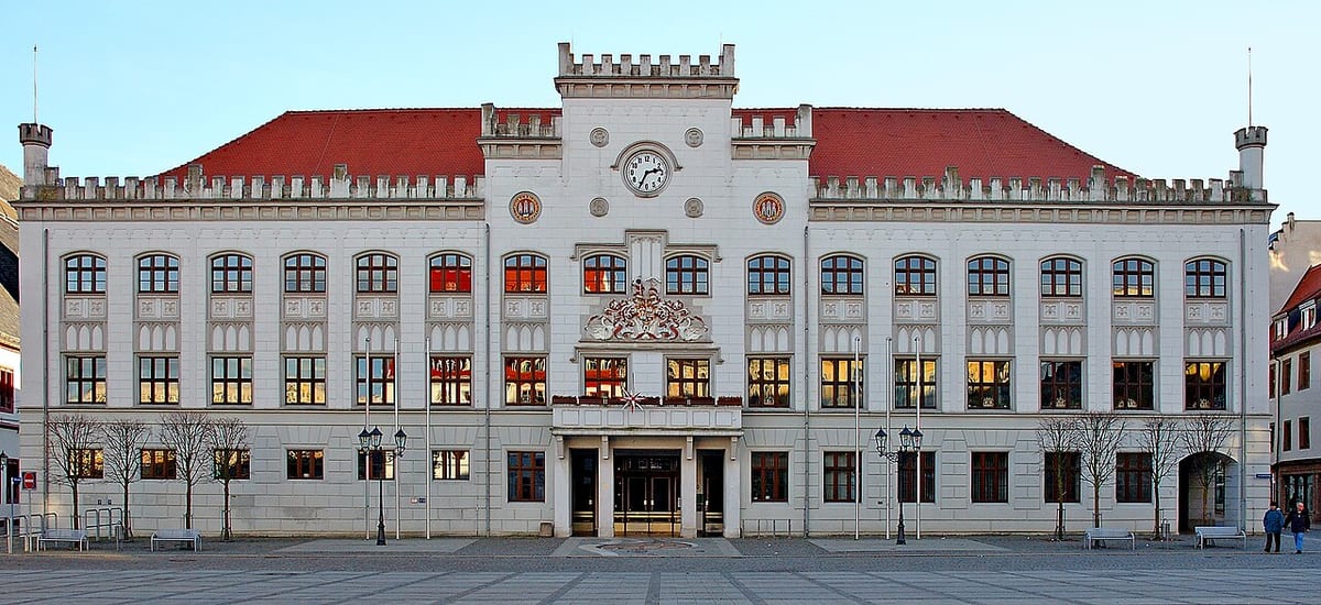 Die symmetrische Front eines historistischen Rathauses mit rotem Dach, frontal aufgenommen