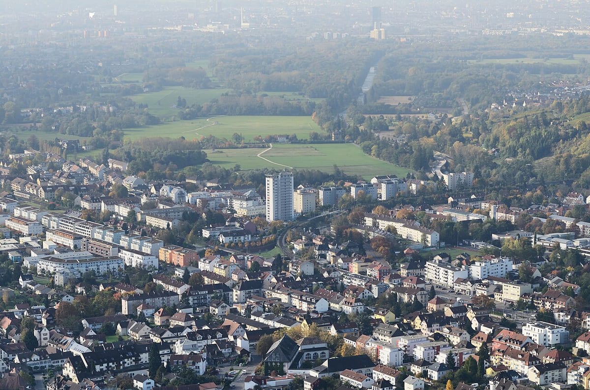 Luftaufnahme über eine Kleinstadt, dahinter Felder und Wald bis zum Horizont